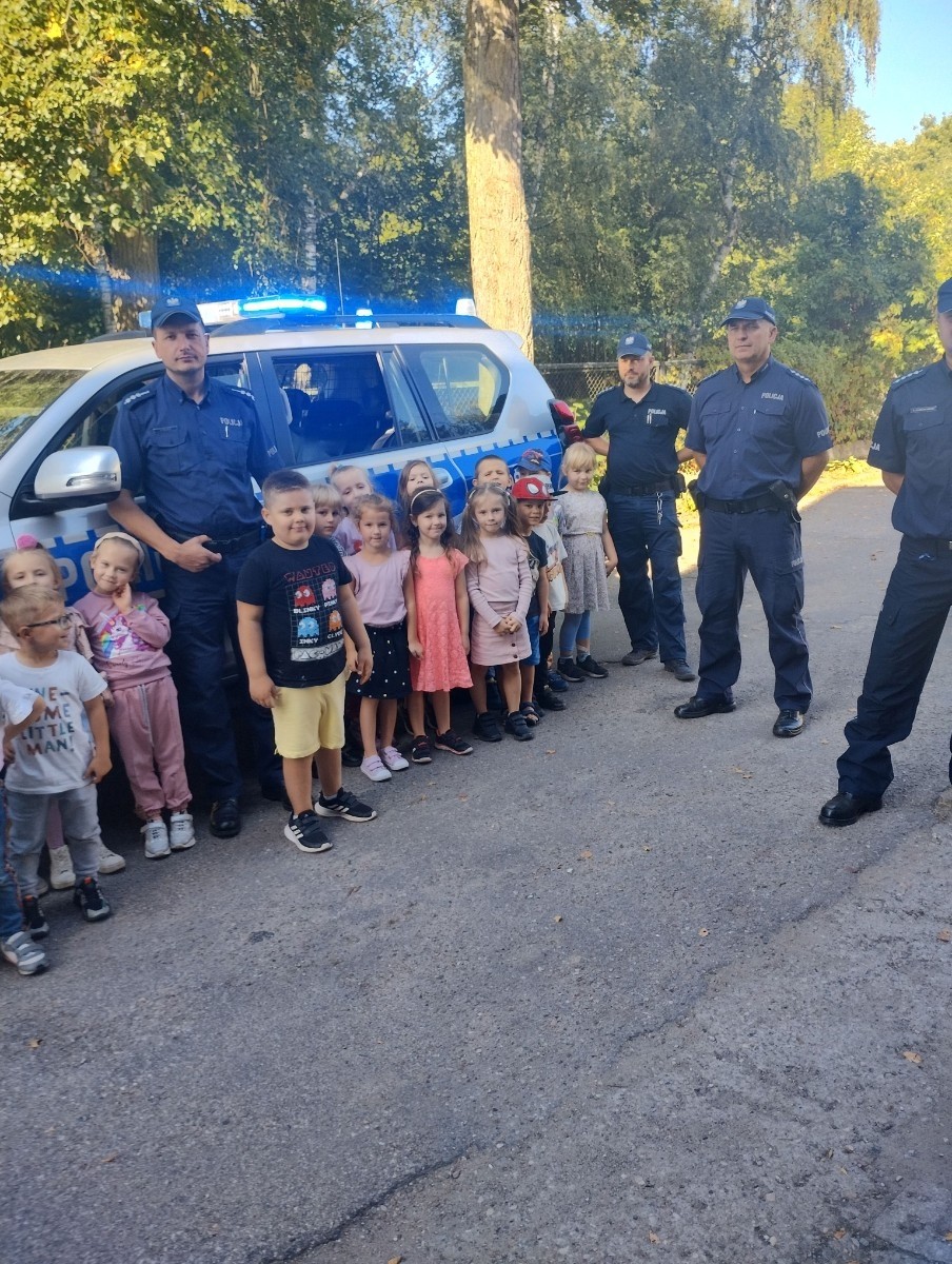 Dnia 28.09.2023r.nasze przedszkolaki miały okazję spotkać się z policjantami. Podczas spotkania przedszkolaki przypomniały sobie zasady bezpiecznego poruszania się po drogach, jak reagować w sytuacjach różnych zagrożeń. Goście ostrzegali też przed osobami nieznajomymi z którymi nie wolno rozmawiać oraz wpuszczać ich do domu. Dzieci wysłuchały policyjnych rad oraz zadawały wiele interesujących pytań. Szczególnym zainteresowaniem wśród dzieci cieszyła się prezentacja wyposażenia policyjnego, niezbędnego podczas wykonywania pracy. Mieliśmy ponadto możliwość obejrzenia krótkich filmików w przedszkolu jak bezpiecznie przejść przez jezdnię oraz jakie numery alarmowe powinien znać każdy, aby wezwać pomocy w razie potrzeby.
Dzieci chętnie wysłuchały opowiadań o codziennej pracy policjanta. Spotkanie przebiegało w bardzo miłej atmosferze. Na zakończenie pan policjant wręczył wszystkim dzieciom sześcioletnim odblaski. 
Serdecznie dziękujemy za miłe spotkanie, to spotkanie oraz treści przekazane na pewno na długo pozostaną w naszej pamięci.