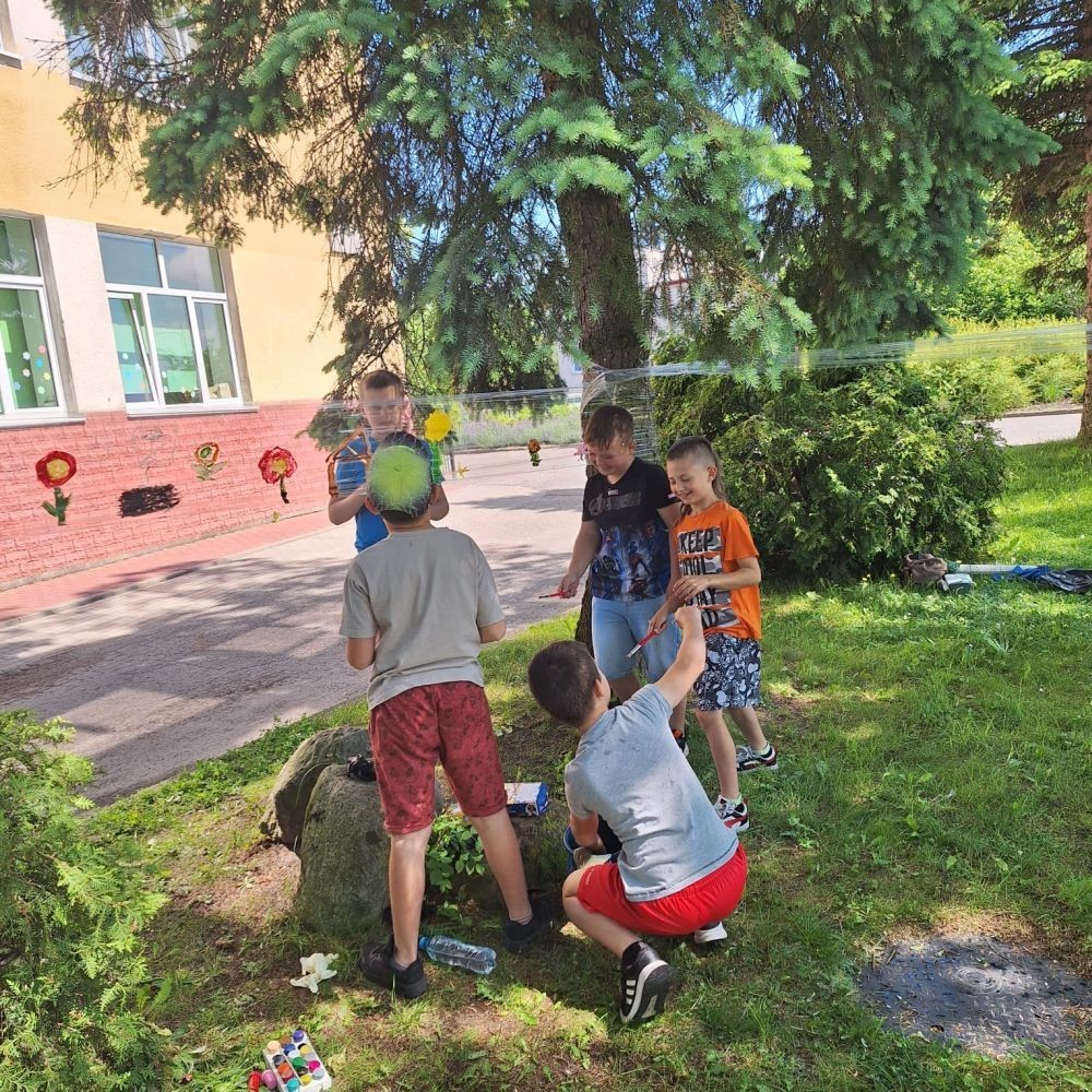 W ostatnim czasie uczniowie klasy III b wzięli udział w wyjątkowych zajęciach plastycznych, które wprawiły ich w zachwyt i radość tworzenia. Tym razem nasze artystyczne dusze miały okazję malować na świeżym powietrzu. Wyjątkowy pomysł na wykorzystanie folii spożywczej rozciągniętej pomiędzy drzewami okazał się strzałem w dziesiątkę. Uczniowie mogli wyrażać swoją kreatywność, eksperymentować z kolorami i formami, czerpiąc inspirację z natury otaczającej naszą szkołę.