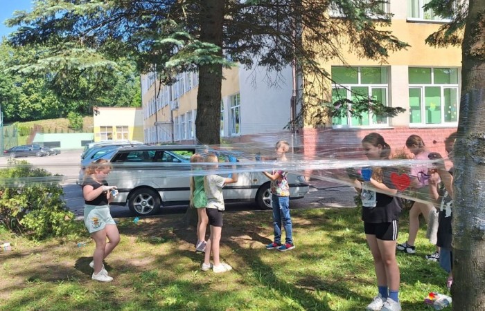 W ostatnim czasie uczniowie klasy III b wzięli udział w wyjątkowych zajęciach plastycznych, które wprawiły ich w zachwyt i radość tworzenia. Tym razem nasze artystyczne dusze miały okazję malować na świeżym powietrzu. Wyjątkowy pomysł na wykorzystanie folii spożywczej rozciągniętej pomiędzy drzewami okazał się strzałem w dziesiątkę. Uczniowie mogli wyrażać swoją kreatywność, eksperymentować z kolorami i formami, czerpiąc inspirację z natury otaczającej naszą szkołę.