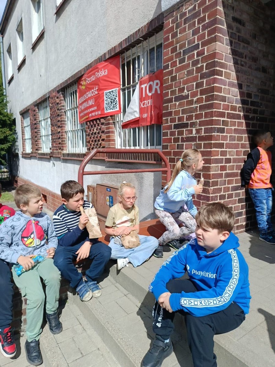 W piątek uczniowie klasy 1a wybrali się na wyjątkową wycieczkę do pobliskiego urzędu pocztowego. Dzieci miały okazję z bliska przyjrzeć się pracy pocztowców, dowiedzieć się, jak wygląda droga listu od nadawcy do adresata, a także zobaczyć, jak działa okienko pocztowe czy stemplowanie przesyłek. Najważniejszym punktem wizyty było jednak coś naprawdę wyjątkowego – uczniowie samodzielnie wysłali listy-niespodzianki z okazji Dnia Mamy. Każda koperta kryła w sobie serce pełne miłości i wdzięczności dla najważniejszych osób w ich życiu.