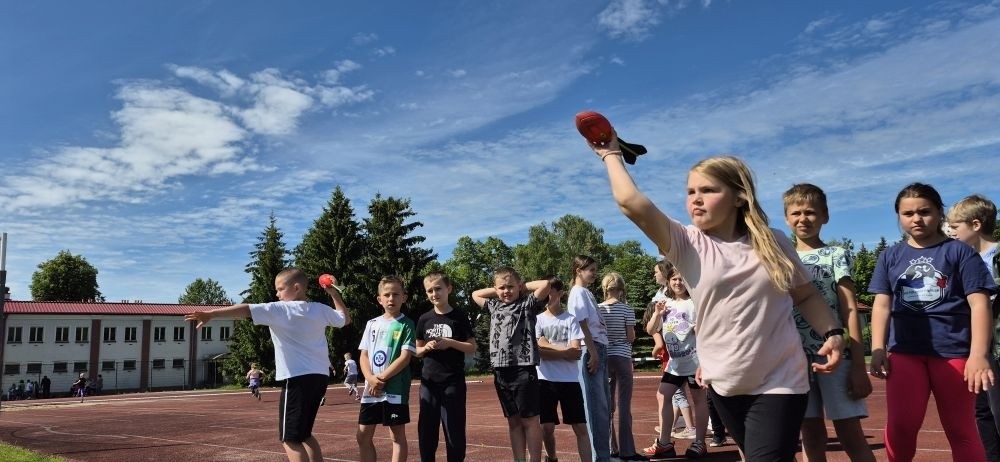 Tegoroczne obchody rozpoczęliśmy twórczo – od przygotowania plakatów „Mistrz zdrowia”. Po tej kreatywnej rozgrzewce przyszedł czas na sportowe emocje. Uroczyste otwarcie było tylko wstępem do licznych atrakcji, które czekały na dzieci na stadionie. Dzięki zaangażowaniu pana Piotra Borysewicza i sportowców z KS Polonia Pasłęk sekcji lekkoatletycznej, uczniowie mogli spróbować swoich sił w biegu przez płotki, rzucie piłeczką oraz torze przeszkód w stylu „Ninja Warrior”. Ogromną atrakcją była również wizyta strażaków z JRG 3 w Pasłęku, którzy zapewnili dzieciom wodno-pianową zabawę. Radość na twarzach uczestników mówiła sama za siebie. Na wszystkich zgłodniałych czekały pyszności, w tym słodka wata cukrowa, serwowana przez Panie z Koła Gospodyń Wiejskich w Borzynowie. Szczególne podziękowania kierujemy do niezastąpionych Rodziców – za wsparcie organizacyjne, opiekę podczas wydarzenia oraz przygotowanie dodatkowych atrakcji: plenerowego studia malowania twarzy i tatuaży. Na zakończenie nikt nie wyszedł z pustymi rękami – niezależnie od wyników konkursów każdy uczeń otrzymał drobny upominek i medal. To wyjątkowe święto pełne radości i zabawy już za nami, więc zaczynamy odliczanie do kolejnego Dnia Dziecka!
