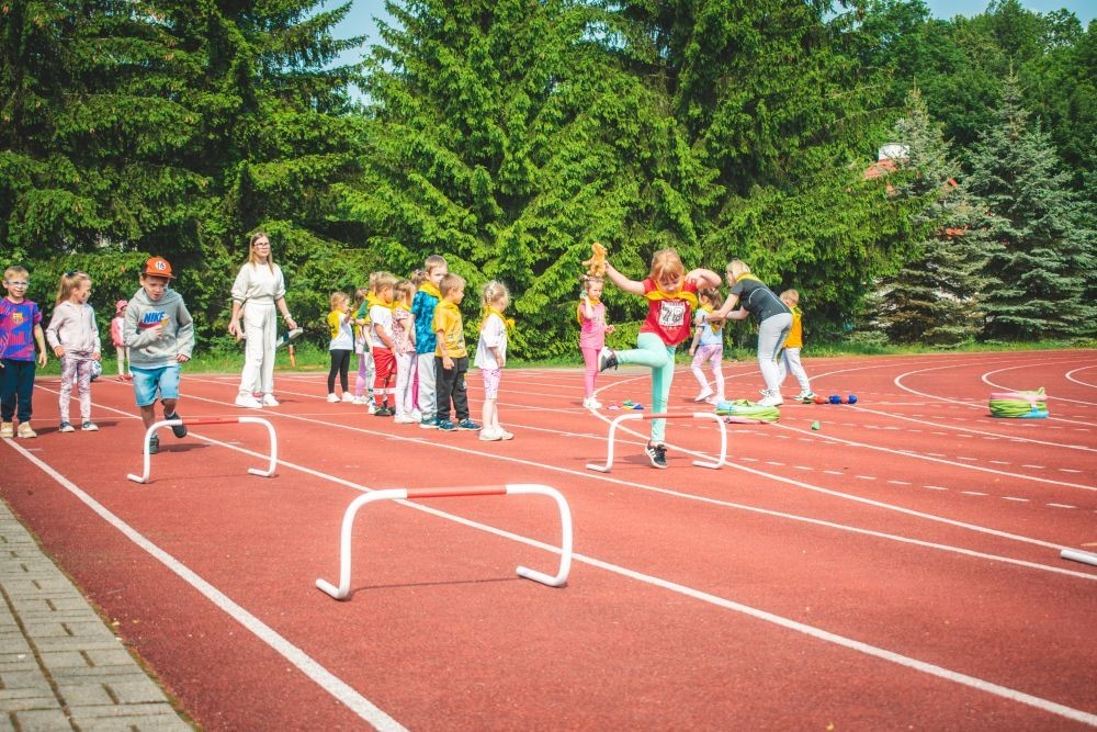 2 czerwca w naszym przedszkolu odbyły się wyjątkowe obchody Dnia Dziecka. W tym roku postawiliśmy na ruch, zabawę i zdrową rywalizację, organizując Sportowy Dzień Dziecka.
Dzień rozpoczęliśmy na Stadionie Miejskim oraz powitania przez panią Dyrektor Agnieszkę Cieklińską i złożenia życzeń z okazji Dnia Dziecka. Następnie wzięliśmy udział w XI edycji Ogólnopolskiego Maratonu Przedszkolaków „Sprintem do maratonu”. Jesteśmy dumne, że nasze przedszkolaki pokonały łącznie aż  3,8 km ! Dalszą część wydarzenia dzieci rywalizowały w różnych konkurencjach: bieg po torze, bieg z przeszkodami, skoki przez płotki czy rzut do celu. Każde dziecko mogło wykazać się sprawnością, zręcznością i współpracą w grupie.
Nie zabrakło także strefy kibica – dzieci dopingowały się nawzajem, a wychowawcy nie szczędzili braw i motywujących okrzyków. Dzięki wsparciu Stowarzyszeniu Przyjaciół Pasłęckiej Dwójki i Koła Gospodyń Wiejskich w Borzynowie w przerwach pomiędzy konkurencjami na dzieci czekały przekąski: owoce, woda, lody, wata cukrowa oraz popcorn.
Na zakończenie wszyscy uczestnicy otrzymali pamiątkowe medale wręczane przez panią Wicedyrektor  Anettę Daszkowską. Radość była ogromna dla dzieci liczyła się przede wszystkim dobra zabawa i wspólnie spędzony czas.
