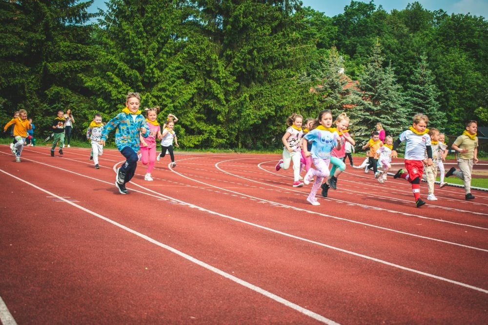 2 czerwca w naszym przedszkolu odbyły się wyjątkowe obchody Dnia Dziecka. W tym roku postawiliśmy na ruch, zabawę i zdrową rywalizację, organizując Sportowy Dzień Dziecka.
Dzień rozpoczęliśmy na Stadionie Miejskim oraz powitania przez panią Dyrektor Agnieszkę Cieklińską i złożenia życzeń z okazji Dnia Dziecka. Następnie wzięliśmy udział w XI edycji Ogólnopolskiego Maratonu Przedszkolaków „Sprintem do maratonu”. Jesteśmy dumne, że nasze przedszkolaki pokonały łącznie aż  3,8 km ! Dalszą część wydarzenia dzieci rywalizowały w różnych konkurencjach: bieg po torze, bieg z przeszkodami, skoki przez płotki czy rzut do celu. Każde dziecko mogło wykazać się sprawnością, zręcznością i współpracą w grupie.
Nie zabrakło także strefy kibica – dzieci dopingowały się nawzajem, a wychowawcy nie szczędzili braw i motywujących okrzyków. Dzięki wsparciu Stowarzyszeniu Przyjaciół Pasłęckiej Dwójki i Koła Gospodyń Wiejskich w Borzynowie w przerwach pomiędzy konkurencjami na dzieci czekały przekąski: owoce, woda, lody, wata cukrowa oraz popcorn.
Na zakończenie wszyscy uczestnicy otrzymali pamiątkowe medale wręczane przez panią Wicedyrektor  Anettę Daszkowską. Radość była ogromna dla dzieci liczyła się przede wszystkim dobra zabawa i wspólnie spędzony czas.
