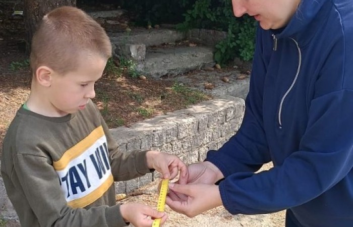 Klasa 1a ruszyła dziś z miarkami krawieckimi na szkolny plac, żeby sprawdzić, ile mierzy… brama, śmietnik i krawężnik. Dzięki praktycznym zajęciom dzieci nie tylko utrwaliły pojęcia związane z długością, ale też świetnie się bawiły mierząc wszystko, co tylko dało się zmierzyć. Takie lekcje to prawdziwa frajda – nauka przez działanie i odkrywanie świata wokół nas.
