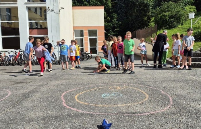 Dziś uczniowie klasy 2b wybrali się na plac przed szkołę, gdzie połączyli przyjemne z pożytecznym. Podczas zabawy w rzuty woreczkiem do celu dzieci nie tylko świetnie się bawiły, ale również ćwiczyły swoją sprawność rachunkową – dodając zdobyte przez grupy punkty.  Radość, ruch i nauka w jednym – właśnie tak lubimy się uczyć.