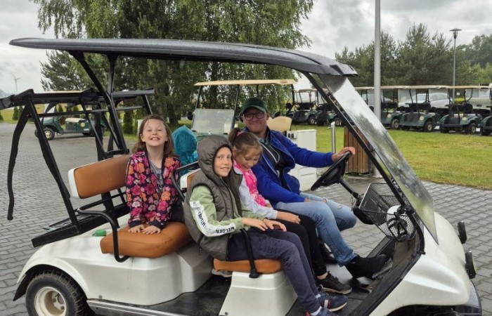 Choć pogoda nie do końca dopisała, uczniowie klasy 2b spędzili niezwykle ciekawy dzień w Sand Valley Golf Resort w Pasłęku. Dzieci miały okazję: dowiedzieć się, na czym polega gra w golfa, obejrzeć profesjonalny sprzęt wykorzystywany w tym sporcie, przejechać się meleksem po rozległym terenie, spróbować pysznych frytek i orzeźwiającej lemoniady serwowanych w tutejszej restauracji. Na zakończenie każdy uczestnik otrzymał pamiątkowy medal, piłeczkę golfową i drobne upominki. Niestety, z powodu deszczu nie udało się przeprowadzić treningu uderzeń piłeczki… ale kto wie – może następnym razem pogoda będzie łaskawsza.