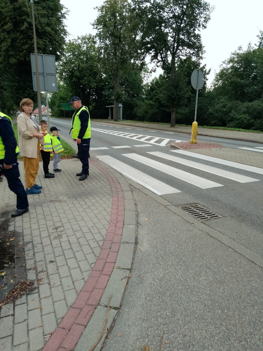 Dzieci z grup starszych Sówki, Leśne skrzaty oraz Biedronki odwiedzili funkcjonariusze policji drogowej , którzy przeprowadzili zajęcia edukacyjne na temat bezpieczeństwa w ruchu ulicznym. Wydarzenie odbyło się w ramach zajęć ,,Moja droga do przedszkola”, której celem jest kształtowanie prawidłowych nawyków i świadomości wśród najmłodszych uczestników ruchu drogowego. Policjanci opowiedzieli przedszkolakom o zasadach bezpiecznego przechodzenia przez jezdnię, znaczeniu znaków drogowych. Dzieci dowiedziały się również, dlaczego ważne jest noszenie odblasków, zwłaszcza jesienią i zimą, gdy wcześniej zapada zmrok.                                
Takie spotkania są bardzo ważne. Dzieci w tym wieku chłoną wiedzę jak gąbka.                  Warto więc już teraz uczyć je zasad, które mogą uratować życie. Przedszkolaki pożegnały policjanta gromkimi brawami i obiecały zawsze pamiętać o zasadach bezpieczeństwa.
Spotkanie z policjantem było nie tylko cenną lekcją, ale też okazją do wzbudzenia w dzieciach zaufania do funkcjonariuszy. To ważny krok w budowaniu poczucia bezpieczeństwa od najmłodszych lat.
