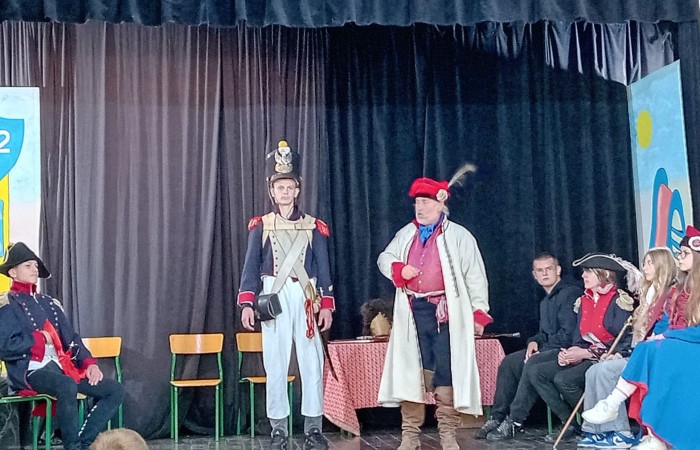 Każdego roku uczniowie naszej szkoły mają niepowtarzalną okazję wziąć udział w wyjątkowym wydarzeniu edukacyjnym - ŻYWEJ LEKCJI HISTORII, prowadzonej przez grupę rekonstrukcyjną Chorągiew Komturstwa Gniewskiego. To spotkanie, które na długo pozostaje w pamięci uczestników, łącząc wiedzę historyczną z emocjami, ruchem i bezpośrednim kontaktem z przeszłością.
W tym roku tematyka spotkań została zrealizowana na dwóch poziomach wiekowych:
Klasy 4-6: Świat starożytnych Greków i Rzymian
Uczniowie klas młodszych przenieśli się do czasów starożytności - epoki potężnych cywilizacji, mitologii, igrzysk olimpijskich i legionów rzymskich. Dzięki strojom z epoki, realistycznym rekwizytom i barwnym opowieściom rekonstruktorów, dzieci mogły poczuć atmosferę antycznego świata. Dowiedzieli się, jak wyglądało życie codzienne Greków i Rzymian, jakie były zwyczaje wojenne, a nawet jak wyglądały ćwiczenia wojskowe legionistów. Zajęcia - prowadzone w formie interaktywnej - dały uczniom możliwość przymierzenia elementów uzbrojenia oraz wzięcia udziału w krótkich pokazach.
Klasy 7-8: Długi wiek XIX
Starsze klasy uczestniczyły w lekcji poświęconej Długiemu wiekowi XIX, czyli okresowi, który ukształtował współczesny świat. Rekonstruktorzy przybliżyli wydarzenia związane z rewolucjami, walką o niepodległość, przemianami społecznymi i narodzinami nowoczesnych idei. Szczególną uwagę poświęcono wydarzeniom ważnym dla Polski - rozbiorom, powstaniom narodowym i postaciom kluczowym dla naszej historii. Uczniowie mogli zobaczyć repliki broni, a także stroje z XIX wieku. Dla wielu była to okazja do poznania historii w sposób bardziej angażujący niż podręcznik - przez opowieści, prezentacje multimedialne i inscenizacje.
Żywa lekcja historii to nie tylko atrakcja, ale przede wszystkim cenna forma nauki. Bezpośredni kontakt z pasjonatami historii oraz aktywne uczestnictwo w przedsięwzięciu sprawia, że uczniowie lepiej zapamiętują materiał, rozbudzają swoją ciekawość i rozwijają szacunek do dziedzictwa kulturowego.