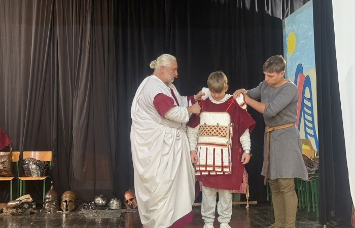 Każdego roku uczniowie naszej szkoły mają niepowtarzalną okazję wziąć udział w wyjątkowym wydarzeniu edukacyjnym - ŻYWEJ LEKCJI HISTORII, prowadzonej przez grupę rekonstrukcyjną Chorągiew Komturstwa Gniewskiego. To spotkanie, które na długo pozostaje w pamięci uczestników, łącząc wiedzę historyczną z emocjami, ruchem i bezpośrednim kontaktem z przeszłością.
W tym roku tematyka spotkań została zrealizowana na dwóch poziomach wiekowych:
Klasy 4-6: Świat starożytnych Greków i Rzymian
Uczniowie klas młodszych przenieśli się do czasów starożytności - epoki potężnych cywilizacji, mitologii, igrzysk olimpijskich i legionów rzymskich. Dzięki strojom z epoki, realistycznym rekwizytom i barwnym opowieściom rekonstruktorów, dzieci mogły poczuć atmosferę antycznego świata. Dowiedzieli się, jak wyglądało życie codzienne Greków i Rzymian, jakie były zwyczaje wojenne, a nawet jak wyglądały ćwiczenia wojskowe legionistów. Zajęcia - prowadzone w formie interaktywnej - dały uczniom możliwość przymierzenia elementów uzbrojenia oraz wzięcia udziału w krótkich pokazach.
Klasy 7-8: Długi wiek XIX
Starsze klasy uczestniczyły w lekcji poświęconej Długiemu wiekowi XIX, czyli okresowi, który ukształtował współczesny świat. Rekonstruktorzy przybliżyli wydarzenia związane z rewolucjami, walką o niepodległość, przemianami społecznymi i narodzinami nowoczesnych idei. Szczególną uwagę poświęcono wydarzeniom ważnym dla Polski - rozbiorom, powstaniom narodowym i postaciom kluczowym dla naszej historii. Uczniowie mogli zobaczyć repliki broni, a także stroje z XIX wieku. Dla wielu była to okazja do poznania historii w sposób bardziej angażujący niż podręcznik - przez opowieści, prezentacje multimedialne i inscenizacje.
Żywa lekcja historii to nie tylko atrakcja, ale przede wszystkim cenna forma nauki. Bezpośredni kontakt z pasjonatami historii oraz aktywne uczestnictwo w przedsięwzięciu sprawia, że uczniowie lepiej zapamiętują materiał, rozbudzają swoją ciekawość i rozwijają szacunek do dziedzictwa kulturowego.