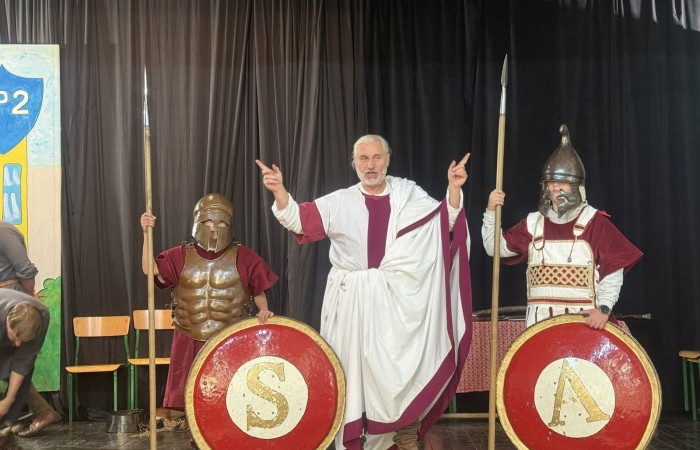 Każdego roku uczniowie naszej szkoły mają niepowtarzalną okazję wziąć udział w wyjątkowym wydarzeniu edukacyjnym - ŻYWEJ LEKCJI HISTORII, prowadzonej przez grupę rekonstrukcyjną Chorągiew Komturstwa Gniewskiego. To spotkanie, które na długo pozostaje w pamięci uczestników, łącząc wiedzę historyczną z emocjami, ruchem i bezpośrednim kontaktem z przeszłością.
W tym roku tematyka spotkań została zrealizowana na dwóch poziomach wiekowych:
Klasy 4-6: Świat starożytnych Greków i Rzymian
Uczniowie klas młodszych przenieśli się do czasów starożytności - epoki potężnych cywilizacji, mitologii, igrzysk olimpijskich i legionów rzymskich. Dzięki strojom z epoki, realistycznym rekwizytom i barwnym opowieściom rekonstruktorów, dzieci mogły poczuć atmosferę antycznego świata. Dowiedzieli się, jak wyglądało życie codzienne Greków i Rzymian, jakie były zwyczaje wojenne, a nawet jak wyglądały ćwiczenia wojskowe legionistów. Zajęcia - prowadzone w formie interaktywnej - dały uczniom możliwość przymierzenia elementów uzbrojenia oraz wzięcia udziału w krótkich pokazach.
Klasy 7-8: Długi wiek XIX
Starsze klasy uczestniczyły w lekcji poświęconej Długiemu wiekowi XIX, czyli okresowi, który ukształtował współczesny świat. Rekonstruktorzy przybliżyli wydarzenia związane z rewolucjami, walką o niepodległość, przemianami społecznymi i narodzinami nowoczesnych idei. Szczególną uwagę poświęcono wydarzeniom ważnym dla Polski - rozbiorom, powstaniom narodowym i postaciom kluczowym dla naszej historii. Uczniowie mogli zobaczyć repliki broni, a także stroje z XIX wieku. Dla wielu była to okazja do poznania historii w sposób bardziej angażujący niż podręcznik - przez opowieści, prezentacje multimedialne i inscenizacje.
Żywa lekcja historii to nie tylko atrakcja, ale przede wszystkim cenna forma nauki. Bezpośredni kontakt z pasjonatami historii oraz aktywne uczestnictwo w przedsięwzięciu sprawia, że uczniowie lepiej zapamiętują materiał, rozbudzają swoją ciekawość i rozwijają szacunek do dziedzictwa kulturowego.