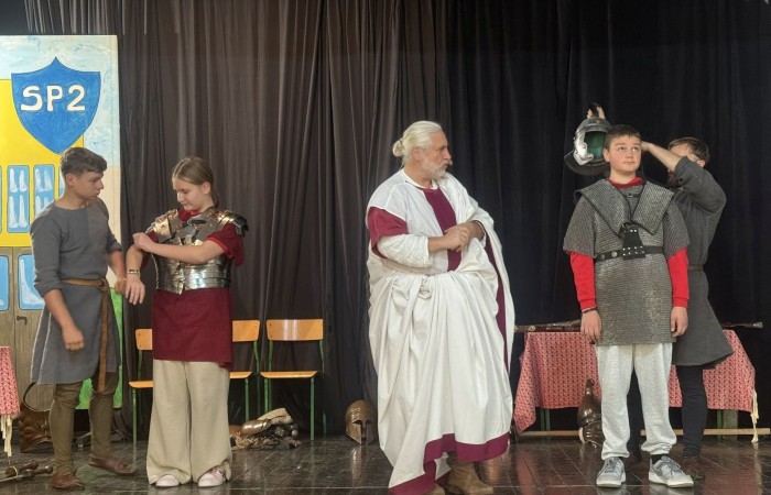 Każdego roku uczniowie naszej szkoły mają niepowtarzalną okazję wziąć udział w wyjątkowym wydarzeniu edukacyjnym - ŻYWEJ LEKCJI HISTORII, prowadzonej przez grupę rekonstrukcyjną Chorągiew Komturstwa Gniewskiego. To spotkanie, które na długo pozostaje w pamięci uczestników, łącząc wiedzę historyczną z emocjami, ruchem i bezpośrednim kontaktem z przeszłością.
W tym roku tematyka spotkań została zrealizowana na dwóch poziomach wiekowych:
Klasy 4-6: Świat starożytnych Greków i Rzymian
Uczniowie klas młodszych przenieśli się do czasów starożytności - epoki potężnych cywilizacji, mitologii, igrzysk olimpijskich i legionów rzymskich. Dzięki strojom z epoki, realistycznym rekwizytom i barwnym opowieściom rekonstruktorów, dzieci mogły poczuć atmosferę antycznego świata. Dowiedzieli się, jak wyglądało życie codzienne Greków i Rzymian, jakie były zwyczaje wojenne, a nawet jak wyglądały ćwiczenia wojskowe legionistów. Zajęcia - prowadzone w formie interaktywnej - dały uczniom możliwość przymierzenia elementów uzbrojenia oraz wzięcia udziału w krótkich pokazach.
Klasy 7-8: Długi wiek XIX
Starsze klasy uczestniczyły w lekcji poświęconej Długiemu wiekowi XIX, czyli okresowi, który ukształtował współczesny świat. Rekonstruktorzy przybliżyli wydarzenia związane z rewolucjami, walką o niepodległość, przemianami społecznymi i narodzinami nowoczesnych idei. Szczególną uwagę poświęcono wydarzeniom ważnym dla Polski - rozbiorom, powstaniom narodowym i postaciom kluczowym dla naszej historii. Uczniowie mogli zobaczyć repliki broni, a także stroje z XIX wieku. Dla wielu była to okazja do poznania historii w sposób bardziej angażujący niż podręcznik - przez opowieści, prezentacje multimedialne i inscenizacje.
Żywa lekcja historii to nie tylko atrakcja, ale przede wszystkim cenna forma nauki. Bezpośredni kontakt z pasjonatami historii oraz aktywne uczestnictwo w przedsięwzięciu sprawia, że uczniowie lepiej zapamiętują materiał, rozbudzają swoją ciekawość i rozwijają szacunek do dziedzictwa kulturowego.