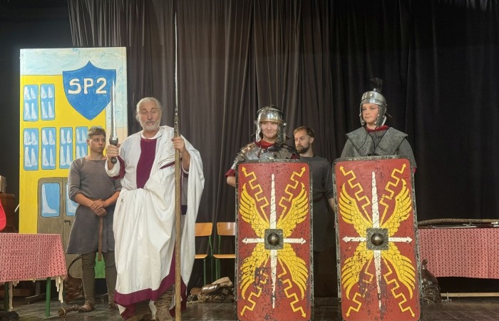 Każdego roku uczniowie naszej szkoły mają niepowtarzalną okazję wziąć udział w wyjątkowym wydarzeniu edukacyjnym - ŻYWEJ LEKCJI HISTORII, prowadzonej przez grupę rekonstrukcyjną Chorągiew Komturstwa Gniewskiego. To spotkanie, które na długo pozostaje w pamięci uczestników, łącząc wiedzę historyczną z emocjami, ruchem i bezpośrednim kontaktem z przeszłością.
W tym roku tematyka spotkań została zrealizowana na dwóch poziomach wiekowych:
Klasy 4-6: Świat starożytnych Greków i Rzymian
Uczniowie klas młodszych przenieśli się do czasów starożytności - epoki potężnych cywilizacji, mitologii, igrzysk olimpijskich i legionów rzymskich. Dzięki strojom z epoki, realistycznym rekwizytom i barwnym opowieściom rekonstruktorów, dzieci mogły poczuć atmosferę antycznego świata. Dowiedzieli się, jak wyglądało życie codzienne Greków i Rzymian, jakie były zwyczaje wojenne, a nawet jak wyglądały ćwiczenia wojskowe legionistów. Zajęcia - prowadzone w formie interaktywnej - dały uczniom możliwość przymierzenia elementów uzbrojenia oraz wzięcia udziału w krótkich pokazach.
Klasy 7-8: Długi wiek XIX
Starsze klasy uczestniczyły w lekcji poświęconej Długiemu wiekowi XIX, czyli okresowi, który ukształtował współczesny świat. Rekonstruktorzy przybliżyli wydarzenia związane z rewolucjami, walką o niepodległość, przemianami społecznymi i narodzinami nowoczesnych idei. Szczególną uwagę poświęcono wydarzeniom ważnym dla Polski - rozbiorom, powstaniom narodowym i postaciom kluczowym dla naszej historii. Uczniowie mogli zobaczyć repliki broni, a także stroje z XIX wieku. Dla wielu była to okazja do poznania historii w sposób bardziej angażujący niż podręcznik - przez opowieści, prezentacje multimedialne i inscenizacje.
Żywa lekcja historii to nie tylko atrakcja, ale przede wszystkim cenna forma nauki. Bezpośredni kontakt z pasjonatami historii oraz aktywne uczestnictwo w przedsięwzięciu sprawia, że uczniowie lepiej zapamiętują materiał, rozbudzają swoją ciekawość i rozwijają szacunek do dziedzictwa kulturowego.