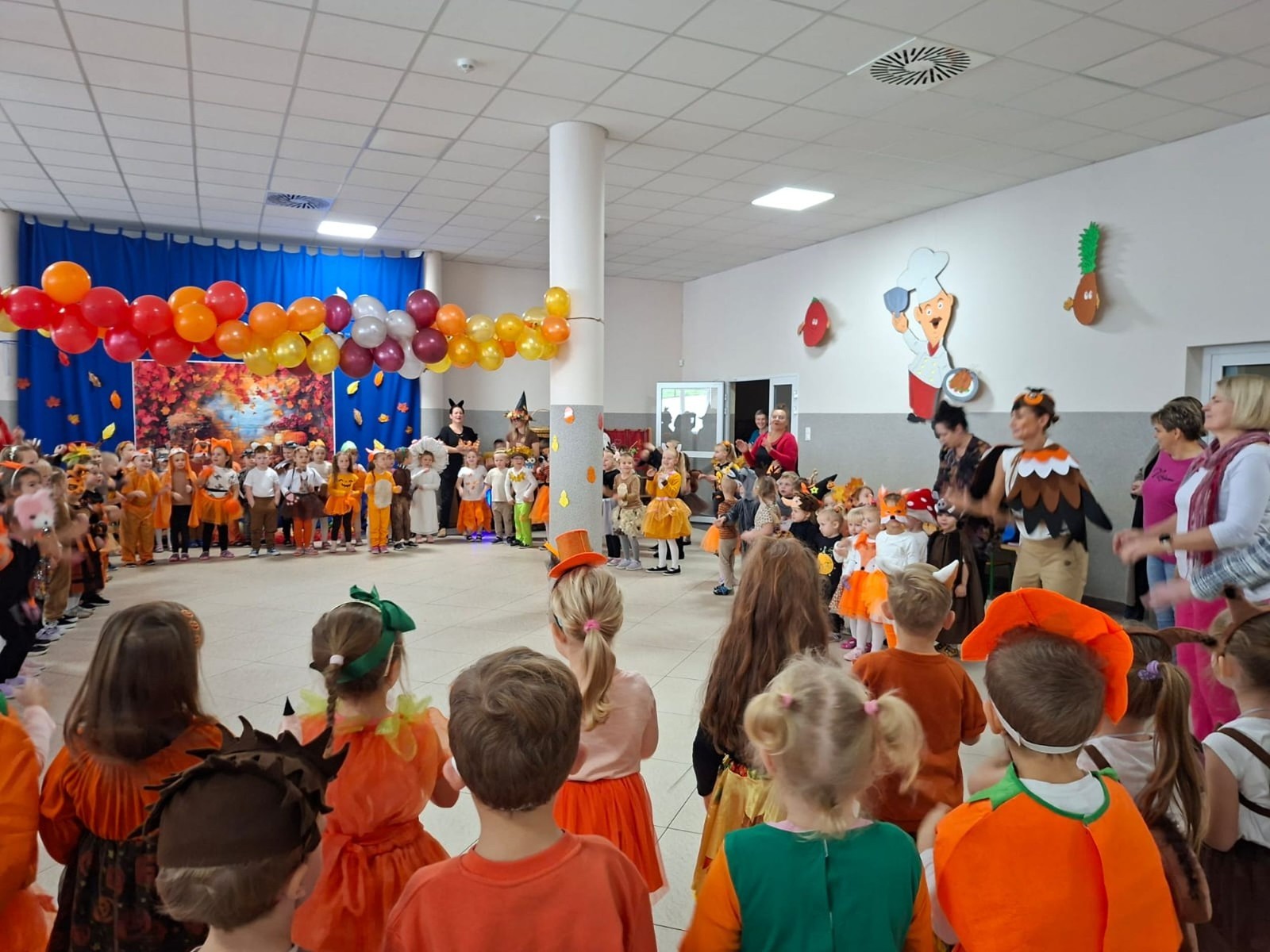 W dniu dzisiejszym w naszym przedszkolu odbył się wyjątkowy i długo wyczekiwany Bal Jesieni. W wydarzeniu wzięły udział wszystkie grupy: Biedronki, Sówki, Leśne Skrzaty oraz Pszczółk oraz dzieci z grup Krasnele i Sówki z Przedszkola Samorządowego nr 1 w Pasłęku, które u nas goszczą od września.
Od samego rana w przedszkolu panowała radosna atmosfera – dzieci przybyły w przepięknych, kolorowych strojach inspirowanych jesienią. Wśród nich można było zobaczyć dynie, jeże, ślimaki, liście, kasztanki, grzybki, wiewiórki, a nawet same Pani Jesienie!
Po powitaniu przez Panie Dyrektor i Wicedyrektor, rozpoczęły się jesienne zabawy i tańce. Wszystkie dzieci wykazały się ogromnym zaangażowaniem, a cała uroczystość odbywała się w duchu radości i wspólnej zabawy.
Nie zabrakło również piosenek i tańców o jesieni – rozbrzmiały takie przeboje z repertuaru dziecięcego Wspólne śpiewanie i tańce przyniosły wszystkim mnóstwo uśmiechu i energii.
Ponadto odbyła się pamiątkowa sesja zdjęciowa w jesiennej scenerii – wśród kolorowych liści, koszy z darami jesieni i szerokich uśmiechów dzieci. 
Jednym z najważniejszych punktów dnia był pokaz jesiennych strojów na niebieskim dywanie. Dzieci z dumą prezentowały swoje przebrania, pozując do zdjęć niczym prawdziwe gwiazdy jesiennego pokazu mody. Publiczność nagradzała ich gromkimi brawami, a w powietrzu czuć było radość i dumę z własnych kreacji.
Bal Jesieni był dniem pełnym barw, muzyki, śmiechu i wspólnej zabawy. Takie wydarzenia integrują dzieci, uczą współpracy, rozwijają kreatywność i pozwalają dostrzec piękno otaczającej nas przyrody. 