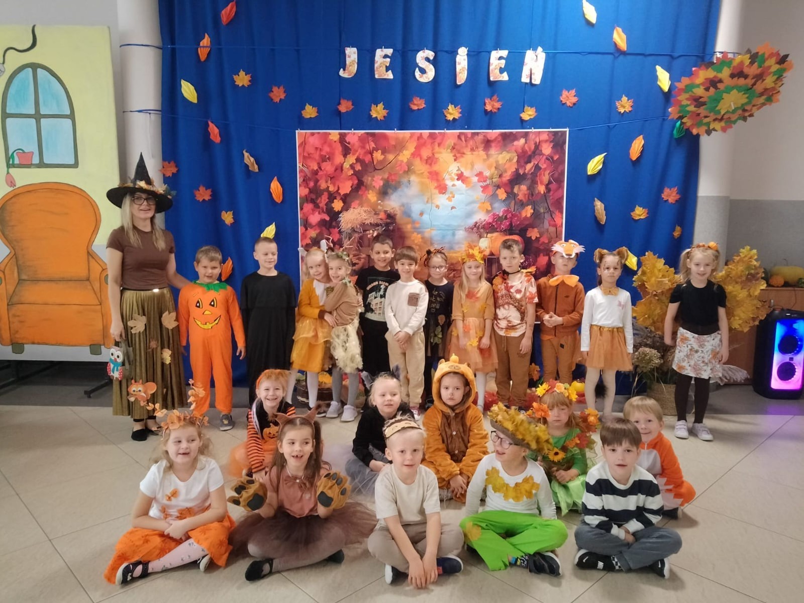 W dniu dzisiejszym w naszym przedszkolu odbył się wyjątkowy i długo wyczekiwany Bal Jesieni. W wydarzeniu wzięły udział wszystkie grupy: Biedronki, Sówki, Leśne Skrzaty oraz Pszczółk oraz dzieci z grup Krasnele i Sówki z Przedszkola Samorządowego nr 1 w Pasłęku, które u nas goszczą od września.
Od samego rana w przedszkolu panowała radosna atmosfera – dzieci przybyły w przepięknych, kolorowych strojach inspirowanych jesienią. Wśród nich można było zobaczyć dynie, jeże, ślimaki, liście, kasztanki, grzybki, wiewiórki, a nawet same Pani Jesienie!
Po powitaniu przez Panie Dyrektor i Wicedyrektor, rozpoczęły się jesienne zabawy i tańce. Wszystkie dzieci wykazały się ogromnym zaangażowaniem, a cała uroczystość odbywała się w duchu radości i wspólnej zabawy.
Nie zabrakło również piosenek i tańców o jesieni – rozbrzmiały takie przeboje z repertuaru dziecięcego Wspólne śpiewanie i tańce przyniosły wszystkim mnóstwo uśmiechu i energii.
Ponadto odbyła się pamiątkowa sesja zdjęciowa w jesiennej scenerii – wśród kolorowych liści, koszy z darami jesieni i szerokich uśmiechów dzieci. 
Jednym z najważniejszych punktów dnia był pokaz jesiennych strojów na niebieskim dywanie. Dzieci z dumą prezentowały swoje przebrania, pozując do zdjęć niczym prawdziwe gwiazdy jesiennego pokazu mody. Publiczność nagradzała ich gromkimi brawami, a w powietrzu czuć było radość i dumę z własnych kreacji.
Bal Jesieni był dniem pełnym barw, muzyki, śmiechu i wspólnej zabawy. Takie wydarzenia integrują dzieci, uczą współpracy, rozwijają kreatywność i pozwalają dostrzec piękno otaczającej nas przyrody. 