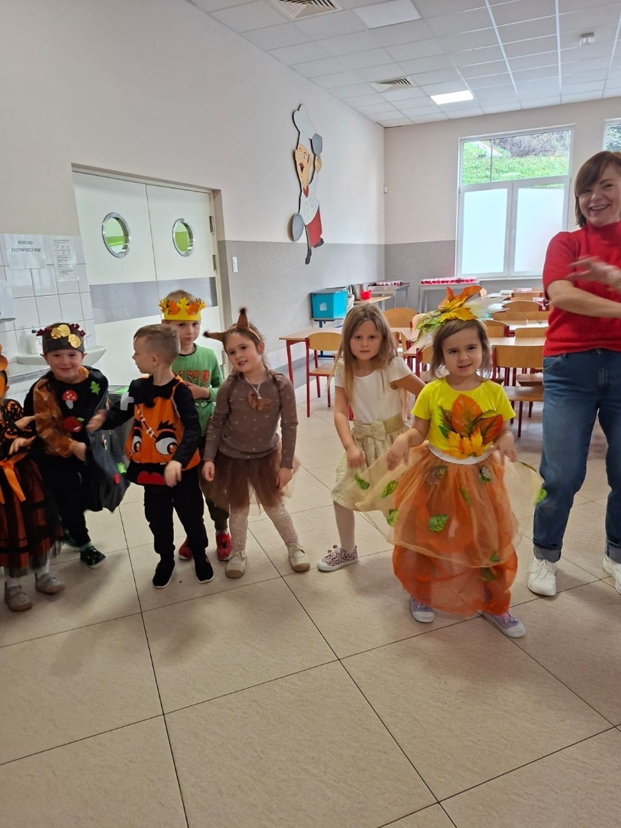 W dniu dzisiejszym w naszym przedszkolu odbył się wyjątkowy i długo wyczekiwany Bal Jesieni. W wydarzeniu wzięły udział wszystkie grupy: Biedronki, Sówki, Leśne Skrzaty oraz Pszczółk oraz dzieci z grup Krasnele i Sówki z Przedszkola Samorządowego nr 1 w Pasłęku, które u nas goszczą od września.
Od samego rana w przedszkolu panowała radosna atmosfera – dzieci przybyły w przepięknych, kolorowych strojach inspirowanych jesienią. Wśród nich można było zobaczyć dynie, jeże, ślimaki, liście, kasztanki, grzybki, wiewiórki, a nawet same Pani Jesienie!
Po powitaniu przez Panie Dyrektor i Wicedyrektor, rozpoczęły się jesienne zabawy i tańce. Wszystkie dzieci wykazały się ogromnym zaangażowaniem, a cała uroczystość odbywała się w duchu radości i wspólnej zabawy.
Nie zabrakło również piosenek i tańców o jesieni – rozbrzmiały takie przeboje z repertuaru dziecięcego Wspólne śpiewanie i tańce przyniosły wszystkim mnóstwo uśmiechu i energii.
Ponadto odbyła się pamiątkowa sesja zdjęciowa w jesiennej scenerii – wśród kolorowych liści, koszy z darami jesieni i szerokich uśmiechów dzieci. 
Jednym z najważniejszych punktów dnia był pokaz jesiennych strojów na niebieskim dywanie. Dzieci z dumą prezentowały swoje przebrania, pozując do zdjęć niczym prawdziwe gwiazdy jesiennego pokazu mody. Publiczność nagradzała ich gromkimi brawami, a w powietrzu czuć było radość i dumę z własnych kreacji.
Bal Jesieni był dniem pełnym barw, muzyki, śmiechu i wspólnej zabawy. Takie wydarzenia integrują dzieci, uczą współpracy, rozwijają kreatywność i pozwalają dostrzec piękno otaczającej nas przyrody. 