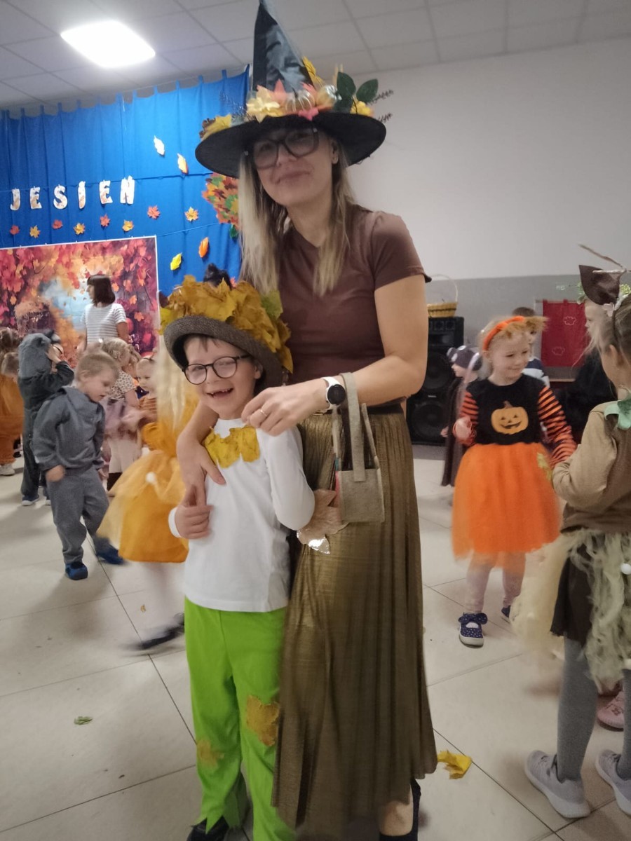 W dniu dzisiejszym w naszym przedszkolu odbył się wyjątkowy i długo wyczekiwany Bal Jesieni. W wydarzeniu wzięły udział wszystkie grupy: Biedronki, Sówki, Leśne Skrzaty oraz Pszczółk oraz dzieci z grup Krasnele i Sówki z Przedszkola Samorządowego nr 1 w Pasłęku, które u nas goszczą od września.
Od samego rana w przedszkolu panowała radosna atmosfera – dzieci przybyły w przepięknych, kolorowych strojach inspirowanych jesienią. Wśród nich można było zobaczyć dynie, jeże, ślimaki, liście, kasztanki, grzybki, wiewiórki, a nawet same Pani Jesienie!
Po powitaniu przez Panie Dyrektor i Wicedyrektor, rozpoczęły się jesienne zabawy i tańce. Wszystkie dzieci wykazały się ogromnym zaangażowaniem, a cała uroczystość odbywała się w duchu radości i wspólnej zabawy.
Nie zabrakło również piosenek i tańców o jesieni – rozbrzmiały takie przeboje z repertuaru dziecięcego Wspólne śpiewanie i tańce przyniosły wszystkim mnóstwo uśmiechu i energii.
Ponadto odbyła się pamiątkowa sesja zdjęciowa w jesiennej scenerii – wśród kolorowych liści, koszy z darami jesieni i szerokich uśmiechów dzieci. 
Jednym z najważniejszych punktów dnia był pokaz jesiennych strojów na niebieskim dywanie. Dzieci z dumą prezentowały swoje przebrania, pozując do zdjęć niczym prawdziwe gwiazdy jesiennego pokazu mody. Publiczność nagradzała ich gromkimi brawami, a w powietrzu czuć było radość i dumę z własnych kreacji.
Bal Jesieni był dniem pełnym barw, muzyki, śmiechu i wspólnej zabawy. Takie wydarzenia integrują dzieci, uczą współpracy, rozwijają kreatywność i pozwalają dostrzec piękno otaczającej nas przyrody. 