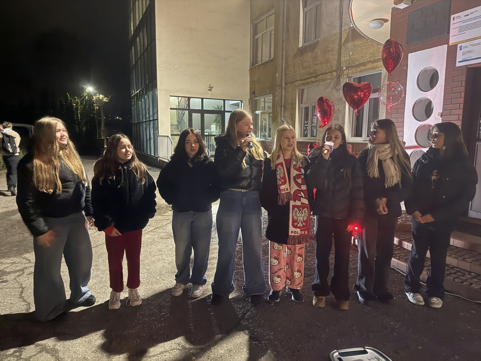 O godzinie 17:00 pod szkołą rozpoczęła się impreza, która zgromadziła około 200 osób. Szkoła została podświetlona na czerwono, co symbolizowało naszą jedność w walce z przemocą. Był to akcent podsumowujący nasze wcześ iej sze  działania w ramach Kampanii Ogólnopolskiej „Dzieciństwo bez Przemocy”. Od października uczniowie uczestniczyli w lekcjach online przygotowanych przez Fundację Dajemy Dzieciom Siłę. Rodzice również zostali objęci wsparciem w postaci webinaru online ww. fudacji.
Uczestnicy mogli wziąć udział w wspólnym śpiewaniu, quizie wiedzy o przemocy oraz tworzeniu „kamieni mocy” – symboli pozytywnej energii i wsparcia. Dodatkowo, w ramach konkursów, przyznano nagrody ufundowane przez Urząd Miejski w Pasłęku.
Ten cudowny czas umilił nam smaczny poczęstunek, w tym grochówka, pizza i ciasta, gorąca kawa i herbatka przygotowany przez panie kucharki i rodziców.
W wydarzeniu uczestniczyli również zaproszeni goście, w tym Burmistrz Pasłęka – pani Elżbieta Wasiuk,  podinspektor KP Pasłęk – pani Agnieszka Bielewicz - Piechowiak oraz przedstawiciel Kuratorium Oświaty w Elblągu – pani Teresa Bednarz, którzy wspierają nasze działania. Ich obecność była dowodem na to, jak ważna jest współpraca lokalnej społeczności w walce z przemocą wobec dzieci. Dziękujemy wszystkim, którzy wzięli udział w tym wyjątkowym dniu oraz przyczynili się do jego organizacji. Razem możemy stworzyć bezpieczne i przyjazne środowisko dla naszych dzieci!
