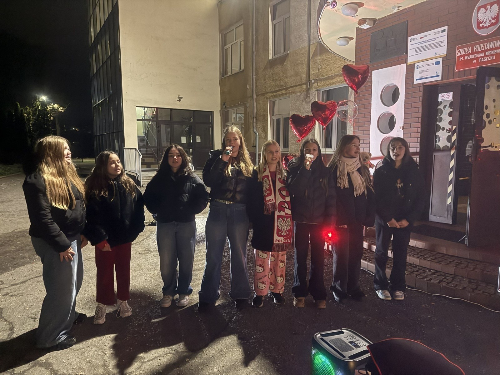 O godzinie 17:00 pod szkołą rozpoczęła się impreza, która zgromadziła około 200 osób. Szkoła została podświetlona na czerwono, co symbolizowało naszą jedność w walce z przemocą. Był to akcent podsumowujący nasze wcześ iej sze  działania w ramach Kampanii Ogólnopolskiej „Dzieciństwo bez Przemocy”. Od października uczniowie uczestniczyli w lekcjach online przygotowanych przez Fundację Dajemy Dzieciom Siłę. Rodzice również zostali objęci wsparciem w postaci webinaru online ww. fudacji.
Uczestnicy mogli wziąć udział w wspólnym śpiewaniu, quizie wiedzy o przemocy oraz tworzeniu „kamieni mocy” – symboli pozytywnej energii i wsparcia. Dodatkowo, w ramach konkursów, przyznano nagrody ufundowane przez Urząd Miejski w Pasłęku.
Ten cudowny czas umilił nam smaczny poczęstunek, w tym grochówka, pizza i ciasta, gorąca kawa i herbatka przygotowany przez panie kucharki i rodziców.
W wydarzeniu uczestniczyli również zaproszeni goście, w tym Burmistrz Pasłęka – pani Elżbieta Wasiuk,  podinspektor KP Pasłęk – pani Agnieszka Bielewicz - Piechowiak oraz przedstawiciel Kuratorium Oświaty w Elblągu – pani Teresa Bednarz, którzy wspierają nasze działania. Ich obecność była dowodem na to, jak ważna jest współpraca lokalnej społeczności w walce z przemocą wobec dzieci. Dziękujemy wszystkim, którzy wzięli udział w tym wyjątkowym dniu oraz przyczynili się do jego organizacji. Razem możemy stworzyć bezpieczne i przyjazne środowisko dla naszych dzieci!
