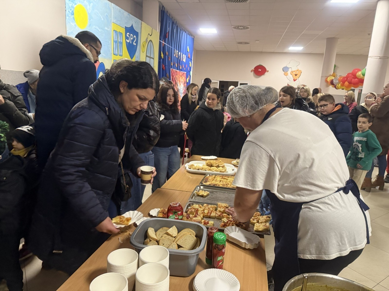 O godzinie 17:00 pod szkołą rozpoczęła się impreza, która zgromadziła około 200 osób. Szkoła została podświetlona na czerwono, co symbolizowało naszą jedność w walce z przemocą. Był to akcent podsumowujący nasze wcześ iej sze  działania w ramach Kampanii Ogólnopolskiej „Dzieciństwo bez Przemocy”. Od października uczniowie uczestniczyli w lekcjach online przygotowanych przez Fundację Dajemy Dzieciom Siłę. Rodzice również zostali objęci wsparciem w postaci webinaru online ww. fudacji.
Uczestnicy mogli wziąć udział w wspólnym śpiewaniu, quizie wiedzy o przemocy oraz tworzeniu „kamieni mocy” – symboli pozytywnej energii i wsparcia. Dodatkowo, w ramach konkursów, przyznano nagrody ufundowane przez Urząd Miejski w Pasłęku.
Ten cudowny czas umilił nam smaczny poczęstunek, w tym grochówka, pizza i ciasta, gorąca kawa i herbatka przygotowany przez panie kucharki i rodziców.
W wydarzeniu uczestniczyli również zaproszeni goście, w tym Burmistrz Pasłęka – pani Elżbieta Wasiuk,  podinspektor KP Pasłęk – pani Agnieszka Bielewicz - Piechowiak oraz przedstawiciel Kuratorium Oświaty w Elblągu – pani Teresa Bednarz, którzy wspierają nasze działania. Ich obecność była dowodem na to, jak ważna jest współpraca lokalnej społeczności w walce z przemocą wobec dzieci. Dziękujemy wszystkim, którzy wzięli udział w tym wyjątkowym dniu oraz przyczynili się do jego organizacji. Razem możemy stworzyć bezpieczne i przyjazne środowisko dla naszych dzieci!
