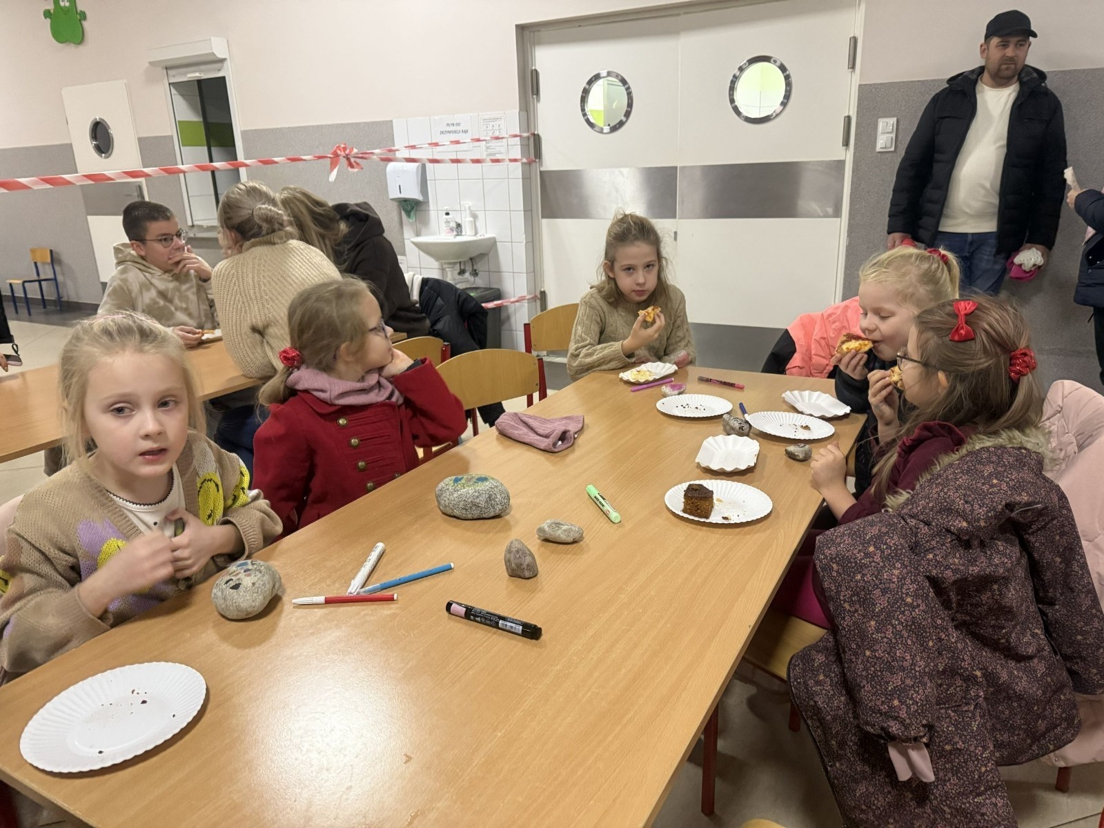 O godzinie 17:00 pod szkołą rozpoczęła się impreza, która zgromadziła około 200 osób. Szkoła została podświetlona na czerwono, co symbolizowało naszą jedność w walce z przemocą. Był to akcent podsumowujący nasze wcześ iej sze  działania w ramach Kampanii Ogólnopolskiej „Dzieciństwo bez Przemocy”. Od października uczniowie uczestniczyli w lekcjach online przygotowanych przez Fundację Dajemy Dzieciom Siłę. Rodzice również zostali objęci wsparciem w postaci webinaru online ww. fudacji.
Uczestnicy mogli wziąć udział w wspólnym śpiewaniu, quizie wiedzy o przemocy oraz tworzeniu „kamieni mocy” – symboli pozytywnej energii i wsparcia. Dodatkowo, w ramach konkursów, przyznano nagrody ufundowane przez Urząd Miejski w Pasłęku.
Ten cudowny czas umilił nam smaczny poczęstunek, w tym grochówka, pizza i ciasta, gorąca kawa i herbatka przygotowany przez panie kucharki i rodziców.
W wydarzeniu uczestniczyli również zaproszeni goście, w tym Burmistrz Pasłęka – pani Elżbieta Wasiuk,  podinspektor KP Pasłęk – pani Agnieszka Bielewicz - Piechowiak oraz przedstawiciel Kuratorium Oświaty w Elblągu – pani Teresa Bednarz, którzy wspierają nasze działania. Ich obecność była dowodem na to, jak ważna jest współpraca lokalnej społeczności w walce z przemocą wobec dzieci. Dziękujemy wszystkim, którzy wzięli udział w tym wyjątkowym dniu oraz przyczynili się do jego organizacji. Razem możemy stworzyć bezpieczne i przyjazne środowisko dla naszych dzieci!
