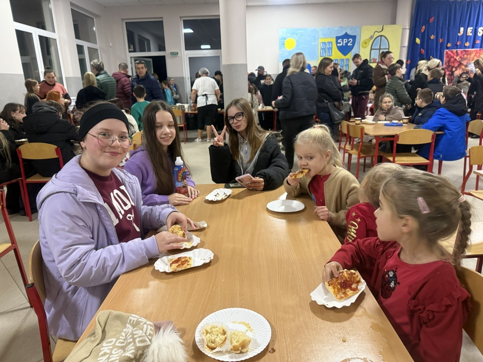 O godzinie 17:00 pod szkołą rozpoczęła się impreza, która zgromadziła około 200 osób. Szkoła została podświetlona na czerwono, co symbolizowało naszą jedność w walce z przemocą. Był to akcent podsumowujący nasze wcześ iej sze  działania w ramach Kampanii Ogólnopolskiej „Dzieciństwo bez Przemocy”. Od października uczniowie uczestniczyli w lekcjach online przygotowanych przez Fundację Dajemy Dzieciom Siłę. Rodzice również zostali objęci wsparciem w postaci webinaru online ww. fudacji.
Uczestnicy mogli wziąć udział w wspólnym śpiewaniu, quizie wiedzy o przemocy oraz tworzeniu „kamieni mocy” – symboli pozytywnej energii i wsparcia. Dodatkowo, w ramach konkursów, przyznano nagrody ufundowane przez Urząd Miejski w Pasłęku.
Ten cudowny czas umilił nam smaczny poczęstunek, w tym grochówka, pizza i ciasta, gorąca kawa i herbatka przygotowany przez panie kucharki i rodziców.
W wydarzeniu uczestniczyli również zaproszeni goście, w tym Burmistrz Pasłęka – pani Elżbieta Wasiuk,  podinspektor KP Pasłęk – pani Agnieszka Bielewicz - Piechowiak oraz przedstawiciel Kuratorium Oświaty w Elblągu – pani Teresa Bednarz, którzy wspierają nasze działania. Ich obecność była dowodem na to, jak ważna jest współpraca lokalnej społeczności w walce z przemocą wobec dzieci. Dziękujemy wszystkim, którzy wzięli udział w tym wyjątkowym dniu oraz przyczynili się do jego organizacji. Razem możemy stworzyć bezpieczne i przyjazne środowisko dla naszych dzieci!
