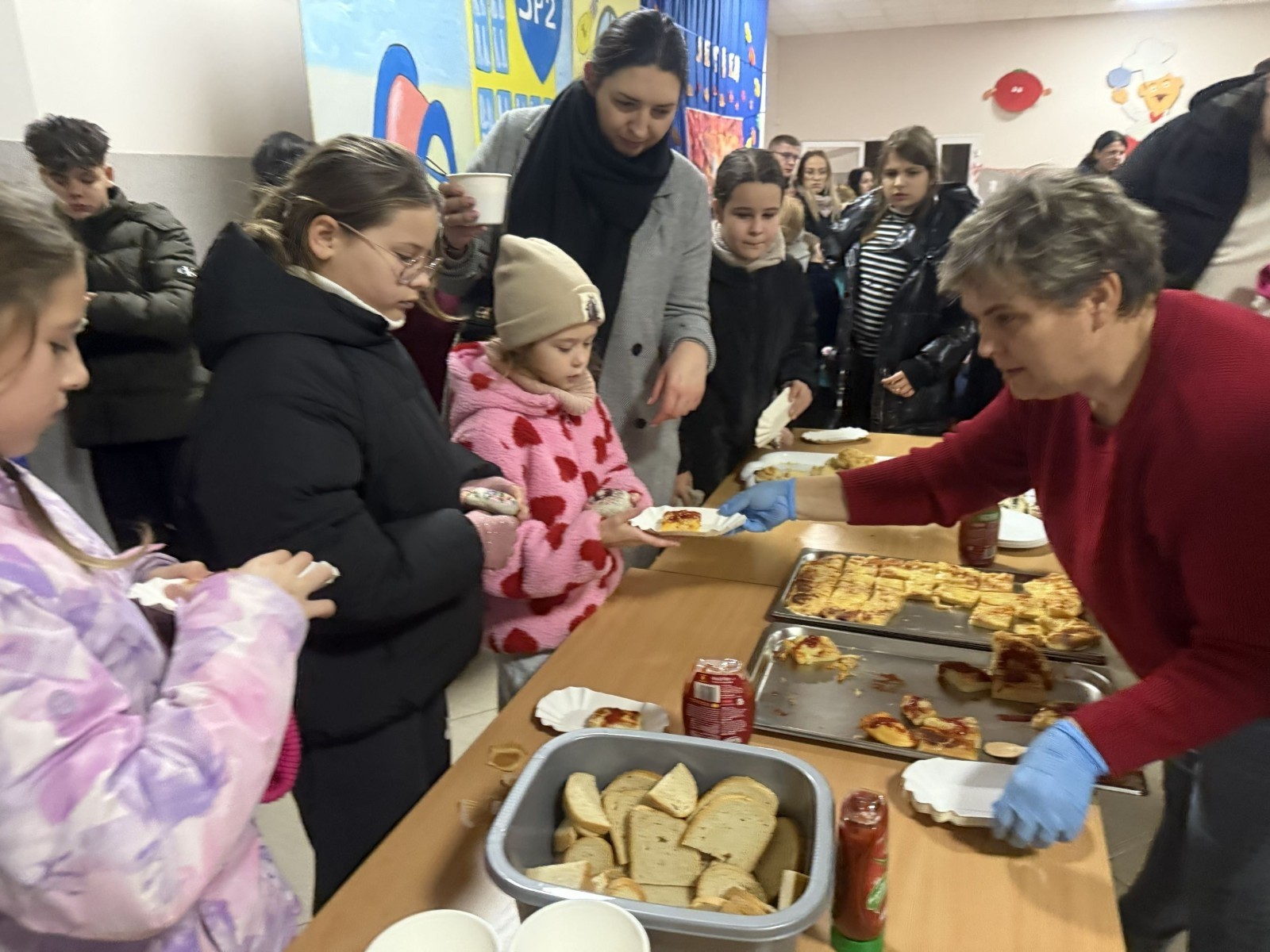 O godzinie 17:00 pod szkołą rozpoczęła się impreza, która zgromadziła około 200 osób. Szkoła została podświetlona na czerwono, co symbolizowało naszą jedność w walce z przemocą. Był to akcent podsumowujący nasze wcześ iej sze  działania w ramach Kampanii Ogólnopolskiej „Dzieciństwo bez Przemocy”. Od października uczniowie uczestniczyli w lekcjach online przygotowanych przez Fundację Dajemy Dzieciom Siłę. Rodzice również zostali objęci wsparciem w postaci webinaru online ww. fudacji.
Uczestnicy mogli wziąć udział w wspólnym śpiewaniu, quizie wiedzy o przemocy oraz tworzeniu „kamieni mocy” – symboli pozytywnej energii i wsparcia. Dodatkowo, w ramach konkursów, przyznano nagrody ufundowane przez Urząd Miejski w Pasłęku.
Ten cudowny czas umilił nam smaczny poczęstunek, w tym grochówka, pizza i ciasta, gorąca kawa i herbatka przygotowany przez panie kucharki i rodziców.
W wydarzeniu uczestniczyli również zaproszeni goście, w tym Burmistrz Pasłęka – pani Elżbieta Wasiuk,  podinspektor KP Pasłęk – pani Agnieszka Bielewicz - Piechowiak oraz przedstawiciel Kuratorium Oświaty w Elblągu – pani Teresa Bednarz, którzy wspierają nasze działania. Ich obecność była dowodem na to, jak ważna jest współpraca lokalnej społeczności w walce z przemocą wobec dzieci. Dziękujemy wszystkim, którzy wzięli udział w tym wyjątkowym dniu oraz przyczynili się do jego organizacji. Razem możemy stworzyć bezpieczne i przyjazne środowisko dla naszych dzieci!
