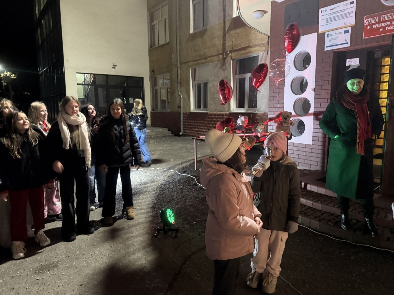 O godzinie 17:00 pod szkołą rozpoczęła się impreza, która zgromadziła około 200 osób. Szkoła została podświetlona na czerwono, co symbolizowało naszą jedność w walce z przemocą. Był to akcent podsumowujący nasze wcześ iej sze  działania w ramach Kampanii Ogólnopolskiej „Dzieciństwo bez Przemocy”. Od października uczniowie uczestniczyli w lekcjach online przygotowanych przez Fundację Dajemy Dzieciom Siłę. Rodzice również zostali objęci wsparciem w postaci webinaru online ww. fudacji.
Uczestnicy mogli wziąć udział w wspólnym śpiewaniu, quizie wiedzy o przemocy oraz tworzeniu „kamieni mocy” – symboli pozytywnej energii i wsparcia. Dodatkowo, w ramach konkursów, przyznano nagrody ufundowane przez Urząd Miejski w Pasłęku.
Ten cudowny czas umilił nam smaczny poczęstunek, w tym grochówka, pizza i ciasta, gorąca kawa i herbatka przygotowany przez panie kucharki i rodziców.
W wydarzeniu uczestniczyli również zaproszeni goście, w tym Burmistrz Pasłęka – pani Elżbieta Wasiuk,  podinspektor KP Pasłęk – pani Agnieszka Bielewicz - Piechowiak oraz przedstawiciel Kuratorium Oświaty w Elblągu – pani Teresa Bednarz, którzy wspierają nasze działania. Ich obecność była dowodem na to, jak ważna jest współpraca lokalnej społeczności w walce z przemocą wobec dzieci. Dziękujemy wszystkim, którzy wzięli udział w tym wyjątkowym dniu oraz przyczynili się do jego organizacji. Razem możemy stworzyć bezpieczne i przyjazne środowisko dla naszych dzieci!
