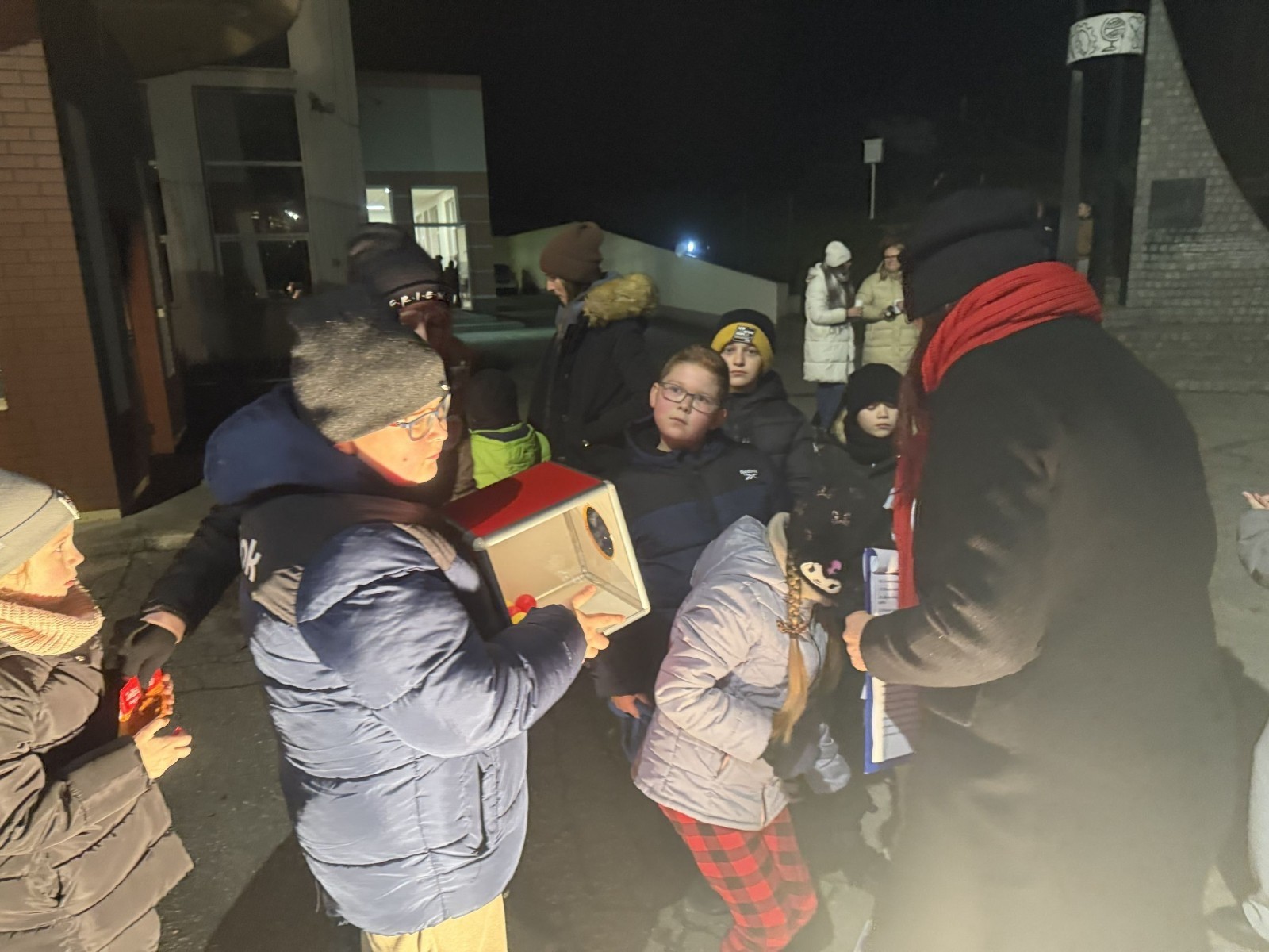 O godzinie 17:00 pod szkołą rozpoczęła się impreza, która zgromadziła około 200 osób. Szkoła została podświetlona na czerwono, co symbolizowało naszą jedność w walce z przemocą. Był to akcent podsumowujący nasze wcześ iej sze  działania w ramach Kampanii Ogólnopolskiej „Dzieciństwo bez Przemocy”. Od października uczniowie uczestniczyli w lekcjach online przygotowanych przez Fundację Dajemy Dzieciom Siłę. Rodzice również zostali objęci wsparciem w postaci webinaru online ww. fudacji.
Uczestnicy mogli wziąć udział w wspólnym śpiewaniu, quizie wiedzy o przemocy oraz tworzeniu „kamieni mocy” – symboli pozytywnej energii i wsparcia. Dodatkowo, w ramach konkursów, przyznano nagrody ufundowane przez Urząd Miejski w Pasłęku.
Ten cudowny czas umilił nam smaczny poczęstunek, w tym grochówka, pizza i ciasta, gorąca kawa i herbatka przygotowany przez panie kucharki i rodziców.
W wydarzeniu uczestniczyli również zaproszeni goście, w tym Burmistrz Pasłęka – pani Elżbieta Wasiuk,  podinspektor KP Pasłęk – pani Agnieszka Bielewicz - Piechowiak oraz przedstawiciel Kuratorium Oświaty w Elblągu – pani Teresa Bednarz, którzy wspierają nasze działania. Ich obecność była dowodem na to, jak ważna jest współpraca lokalnej społeczności w walce z przemocą wobec dzieci. Dziękujemy wszystkim, którzy wzięli udział w tym wyjątkowym dniu oraz przyczynili się do jego organizacji. Razem możemy stworzyć bezpieczne i przyjazne środowisko dla naszych dzieci!
