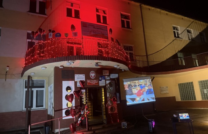 O godzinie 17:00 pod szkołą rozpoczęła się impreza, która zgromadziła około 200 osób. Szkoła została podświetlona na czerwono, co symbolizowało naszą jedność w walce z przemocą. Był to akcent podsumowujący nasze wcześ iej sze  działania w ramach Kampanii Ogólnopolskiej „Dzieciństwo bez Przemocy”. Od października uczniowie uczestniczyli w lekcjach online przygotowanych przez Fundację Dajemy Dzieciom Siłę. Rodzice również zostali objęci wsparciem w postaci webinaru online ww. fudacji.
Uczestnicy mogli wziąć udział w wspólnym śpiewaniu, quizie wiedzy o przemocy oraz tworzeniu „kamieni mocy” – symboli pozytywnej energii i wsparcia. Dodatkowo, w ramach konkursów, przyznano nagrody ufundowane przez Urząd Miejski w Pasłęku.
Ten cudowny czas umilił nam smaczny poczęstunek, w tym grochówka, pizza i ciasta, gorąca kawa i herbatka przygotowany przez panie kucharki i rodziców.
W wydarzeniu uczestniczyli również zaproszeni goście, w tym Burmistrz Pasłęka – pani Elżbieta Wasiuk,  podinspektor KP Pasłęk – pani Agnieszka Bielewicz - Piechowiak oraz przedstawiciel Kuratorium Oświaty w Elblągu – pani Teresa Bednarz, którzy wspierają nasze działania. Ich obecność była dowodem na to, jak ważna jest współpraca lokalnej społeczności w walce z przemocą wobec dzieci. Dziękujemy wszystkim, którzy wzięli udział w tym wyjątkowym dniu oraz przyczynili się do jego organizacji. Razem możemy stworzyć bezpieczne i przyjazne środowisko dla naszych dzieci!
