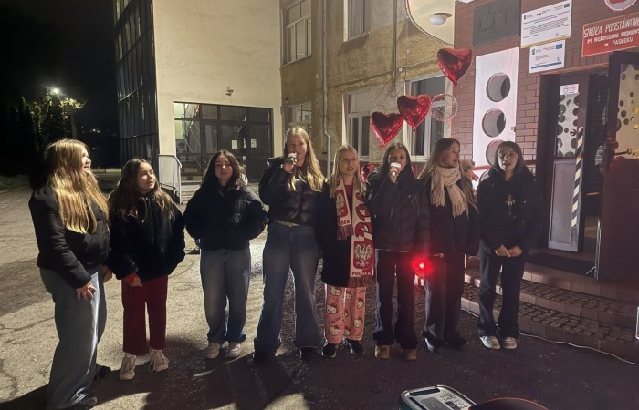 O godzinie 17:00 pod szkołą rozpoczęła się impreza, która zgromadziła około 200 osób. Szkoła została podświetlona na czerwono, co symbolizowało naszą jedność w walce z przemocą. Był to akcent podsumowujący nasze wcześ iej sze  działania w ramach Kampanii Ogólnopolskiej „Dzieciństwo bez Przemocy”. Od października uczniowie uczestniczyli w lekcjach online przygotowanych przez Fundację Dajemy Dzieciom Siłę. Rodzice również zostali objęci wsparciem w postaci webinaru online ww. fudacji.
Uczestnicy mogli wziąć udział w wspólnym śpiewaniu, quizie wiedzy o przemocy oraz tworzeniu „kamieni mocy” – symboli pozytywnej energii i wsparcia. Dodatkowo, w ramach konkursów, przyznano nagrody ufundowane przez Urząd Miejski w Pasłęku.
Ten cudowny czas umilił nam smaczny poczęstunek, w tym grochówka, pizza i ciasta, gorąca kawa i herbatka przygotowany przez panie kucharki i rodziców.
W wydarzeniu uczestniczyli również zaproszeni goście, w tym Burmistrz Pasłęka – pani Elżbieta Wasiuk,  podinspektor KP Pasłęk – pani Agnieszka Bielewicz - Piechowiak oraz przedstawiciel Kuratorium Oświaty w Elblągu – pani Teresa Bednarz, którzy wspierają nasze działania. Ich obecność była dowodem na to, jak ważna jest współpraca lokalnej społeczności w walce z przemocą wobec dzieci. Dziękujemy wszystkim, którzy wzięli udział w tym wyjątkowym dniu oraz przyczynili się do jego organizacji. Razem możemy stworzyć bezpieczne i przyjazne środowisko dla naszych dzieci!
