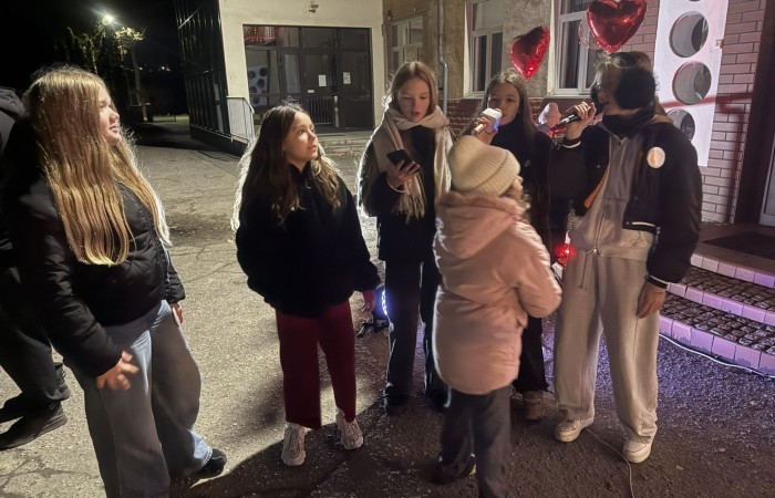 O godzinie 17:00 pod szkołą rozpoczęła się impreza, która zgromadziła około 200 osób. Szkoła została podświetlona na czerwono, co symbolizowało naszą jedność w walce z przemocą. Był to akcent podsumowujący nasze wcześ iej sze  działania w ramach Kampanii Ogólnopolskiej „Dzieciństwo bez Przemocy”. Od października uczniowie uczestniczyli w lekcjach online przygotowanych przez Fundację Dajemy Dzieciom Siłę. Rodzice również zostali objęci wsparciem w postaci webinaru online ww. fudacji.
Uczestnicy mogli wziąć udział w wspólnym śpiewaniu, quizie wiedzy o przemocy oraz tworzeniu „kamieni mocy” – symboli pozytywnej energii i wsparcia. Dodatkowo, w ramach konkursów, przyznano nagrody ufundowane przez Urząd Miejski w Pasłęku.
Ten cudowny czas umilił nam smaczny poczęstunek, w tym grochówka, pizza i ciasta, gorąca kawa i herbatka przygotowany przez panie kucharki i rodziców.
W wydarzeniu uczestniczyli również zaproszeni goście, w tym Burmistrz Pasłęka – pani Elżbieta Wasiuk,  podinspektor KP Pasłęk – pani Agnieszka Bielewicz - Piechowiak oraz przedstawiciel Kuratorium Oświaty w Elblągu – pani Teresa Bednarz, którzy wspierają nasze działania. Ich obecność była dowodem na to, jak ważna jest współpraca lokalnej społeczności w walce z przemocą wobec dzieci. Dziękujemy wszystkim, którzy wzięli udział w tym wyjątkowym dniu oraz przyczynili się do jego organizacji. Razem możemy stworzyć bezpieczne i przyjazne środowisko dla naszych dzieci!
