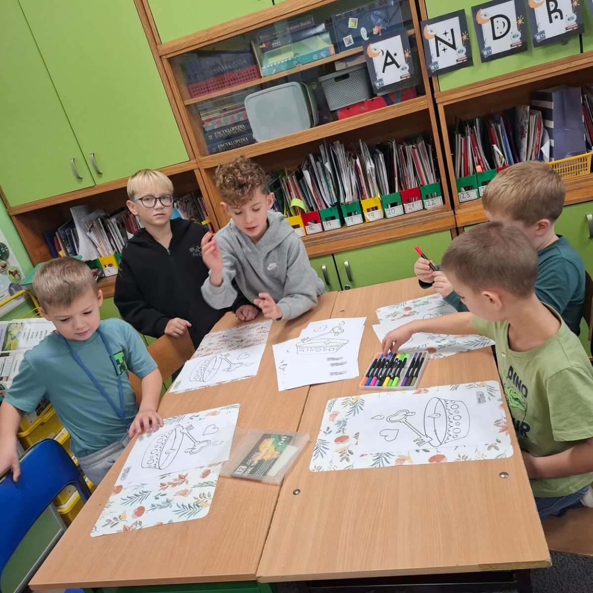 W tym roku Andrzejki w naszej szkole były pełne magii, radości i uśmiechu. Uczniowie klas trzecich przygotowali dla pierwszaków wyjątkowe wróżby i zabawy, dzięki którym mali uczestnicy mogli poczuć prawdziwą andrzejkową atmosferę. Nie zabrakło tradycyjnych wróżb, takich jak serca z imionami, magiczne kubeczki czy karty, a także mnóstwa śmiechu i wspólnej zabawy. Było kolorowo, wesoło i… trochę tajemniczo.
Serdeczne podziękowania dla naszych starszych uczniów za kreatywność i świetną zabawę, a także dla pierwszaków za aktywny udział w andrzejkowych atrakcjach. To był naprawdę magiczny dzień.